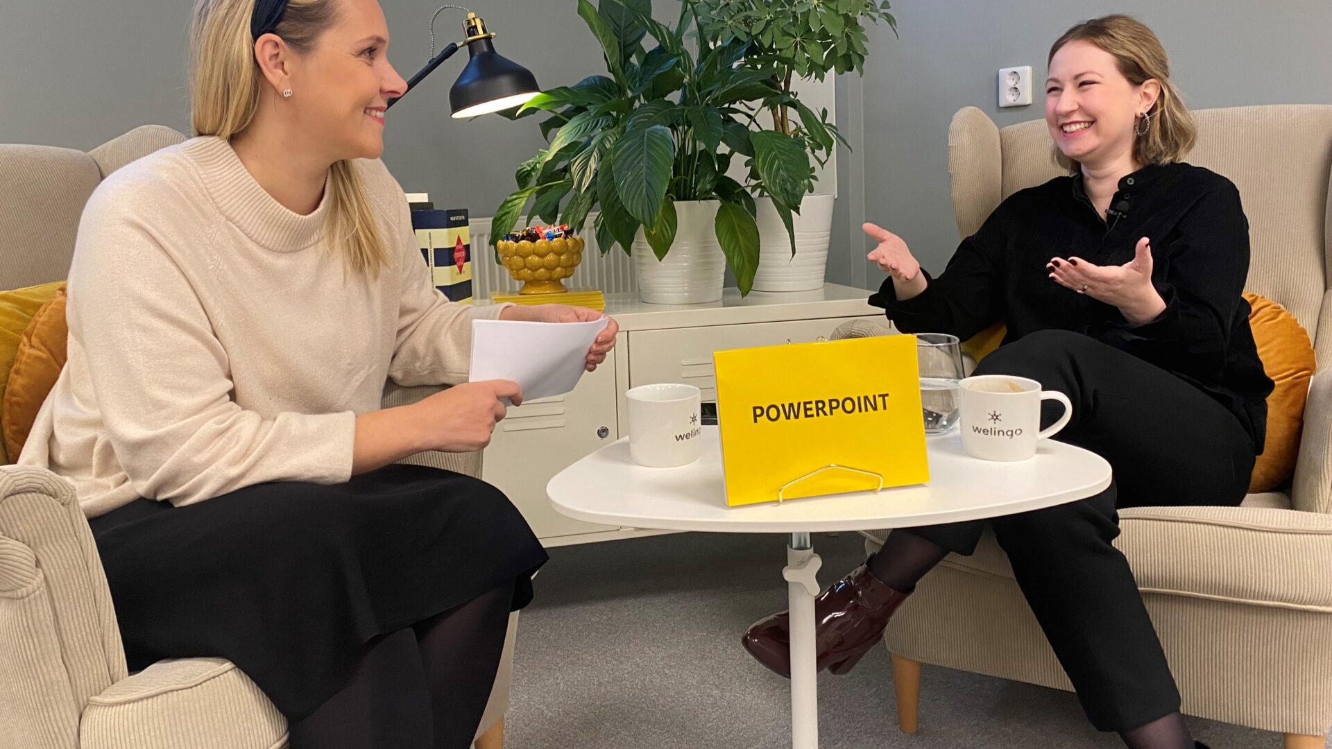Två personer sitter i varsin fåtölj. En skylt på bordet visar att de pratar om PowerPoint.