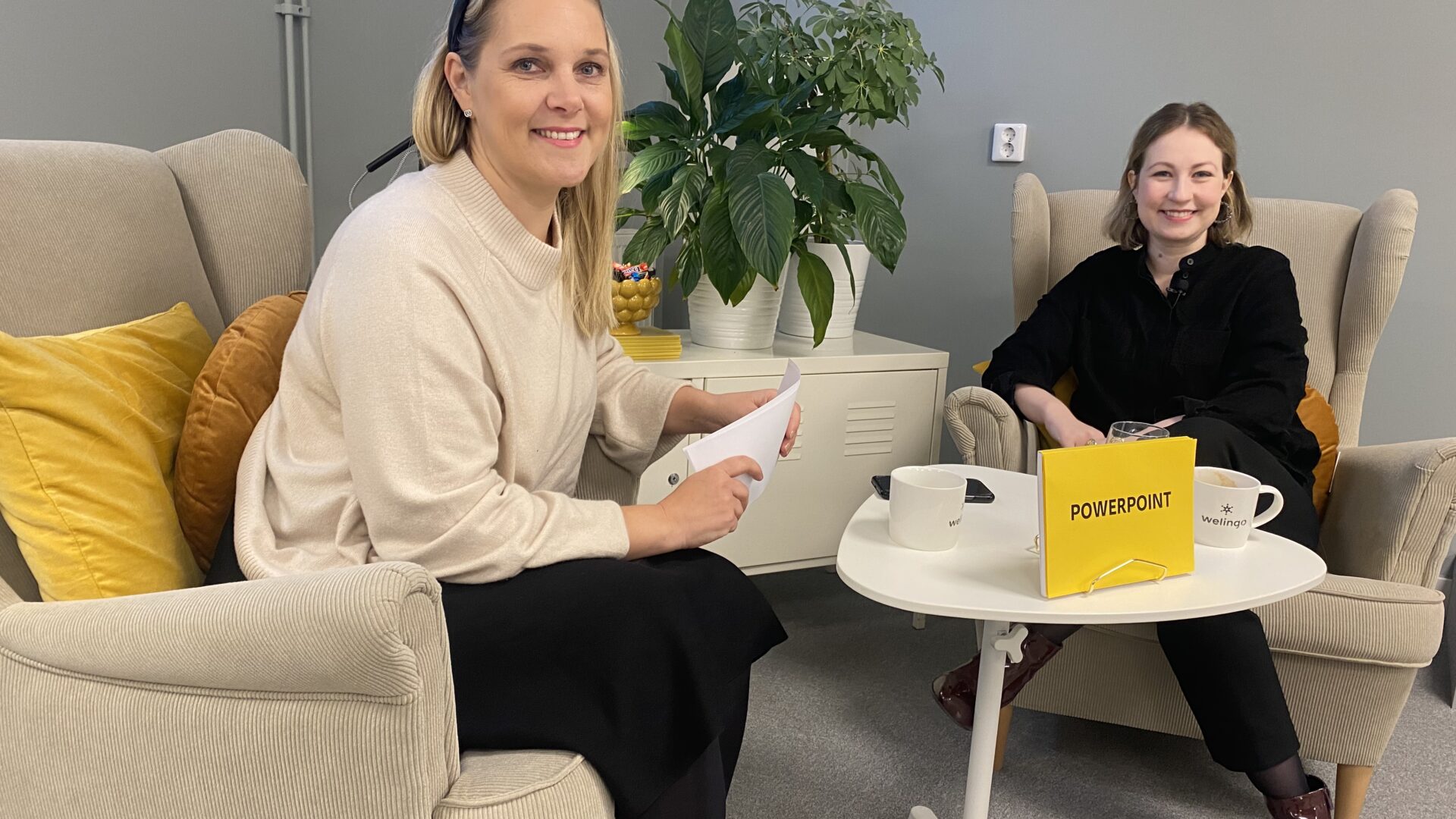Två personer, som båda tittar in i kameran, sitter i varsin fåtölj. En skylt på bordet visar att de pratar om PowerPoint.