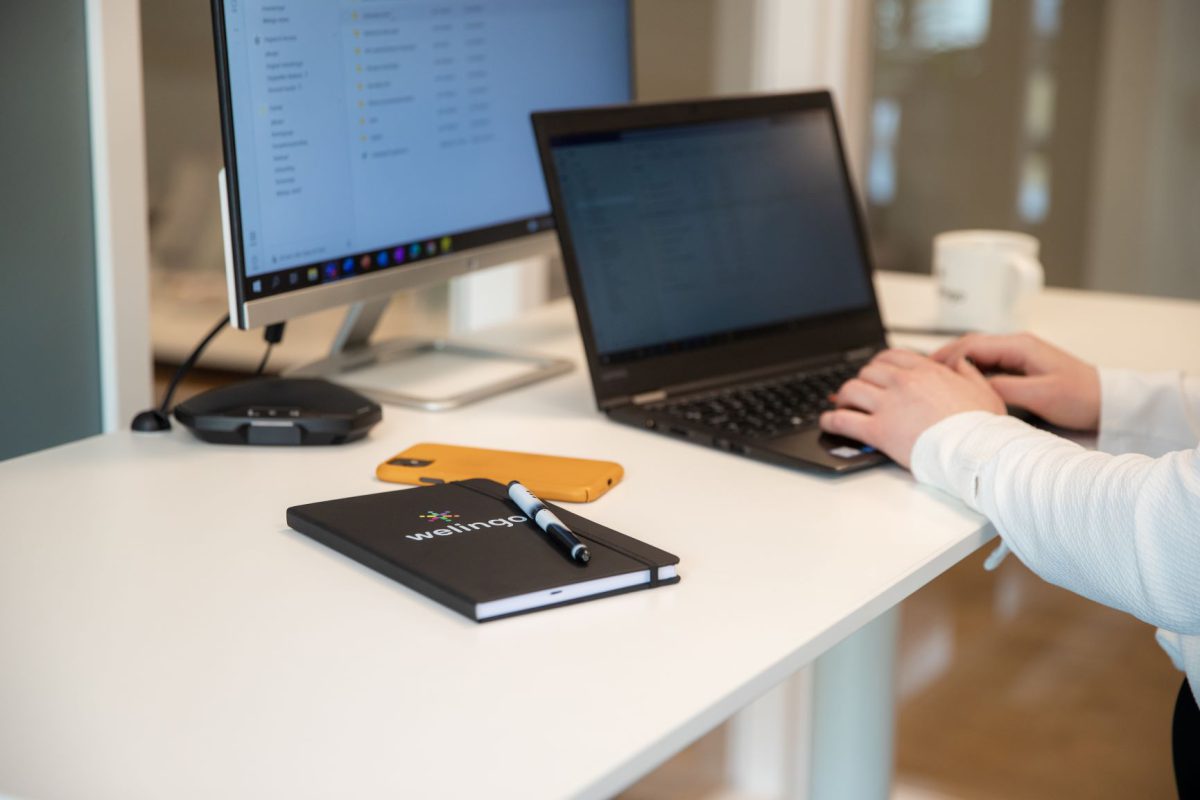 Närbild på ett par händer som arbetar med en laptop. På bordet syns också ett skrivblock med Welingos logga.